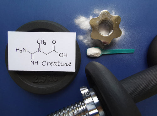 Chemical formula for creatine, a creatine scoop, and a few weights displayed in a gym setting.